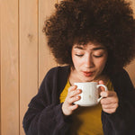 Woman enjoying a warm cup of Shadow Work coffee in a white porcelain mug against a wooden background