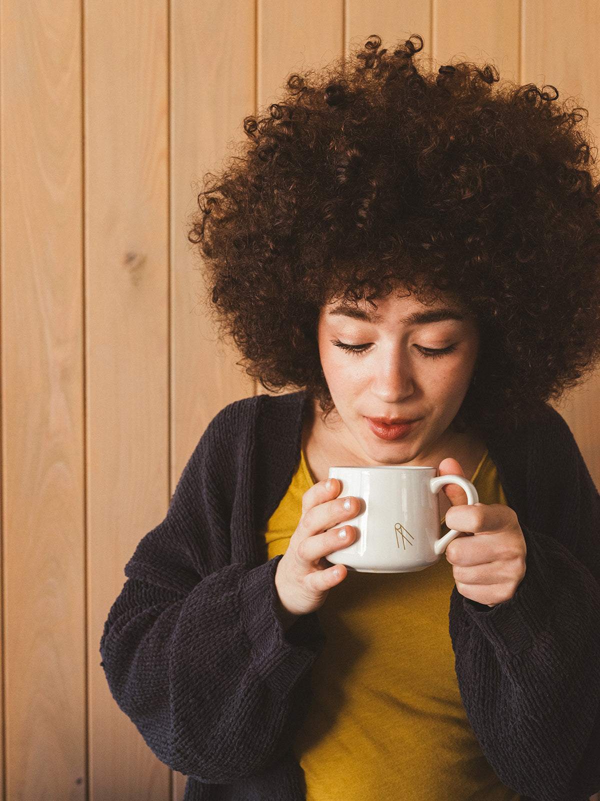 Woman enjoying a warm cup of Shadow Work coffee in a white porcelain mug against a wooden background