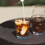 Luna Nueva specialty-grade Mexican coffee with cream being poured into iced coffee in clear glasses on black surface