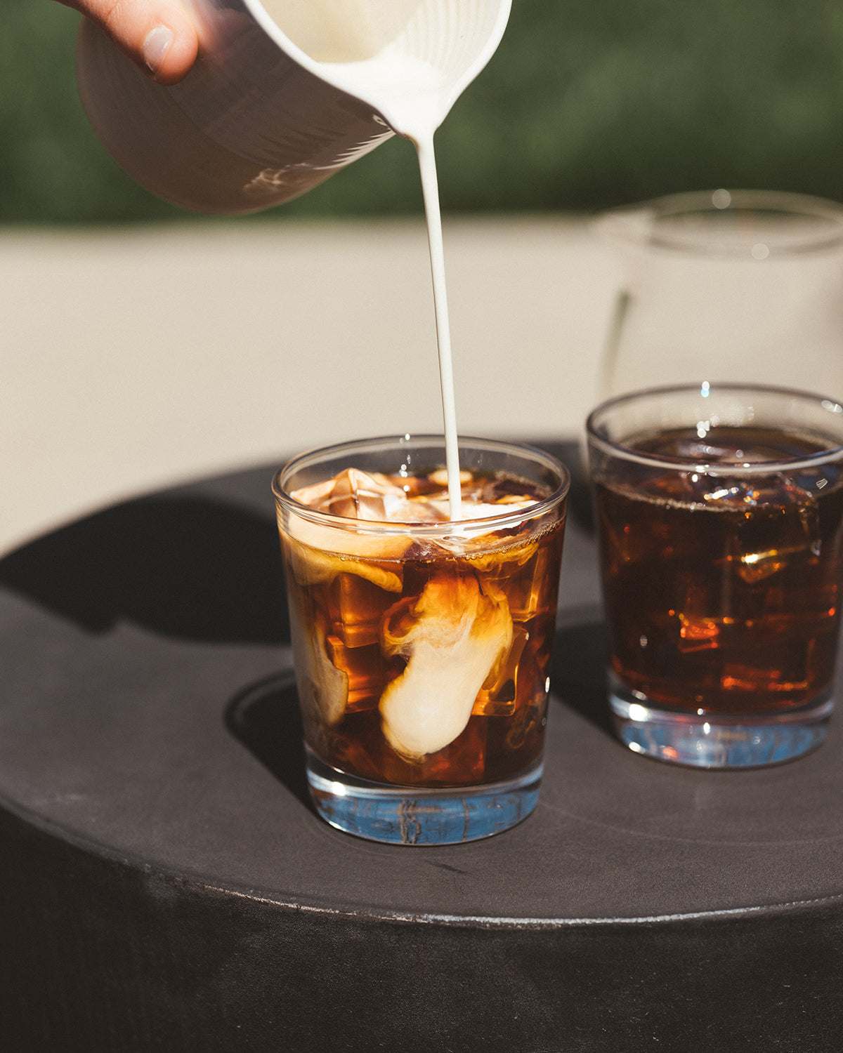 Luna Nueva specialty-grade Mexican coffee with cream being poured into iced coffee in clear glasses on black surface