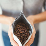 Close-up of a person holding an open bag of Shadow Work coffee beans showcasing rich, roasted beans inside.