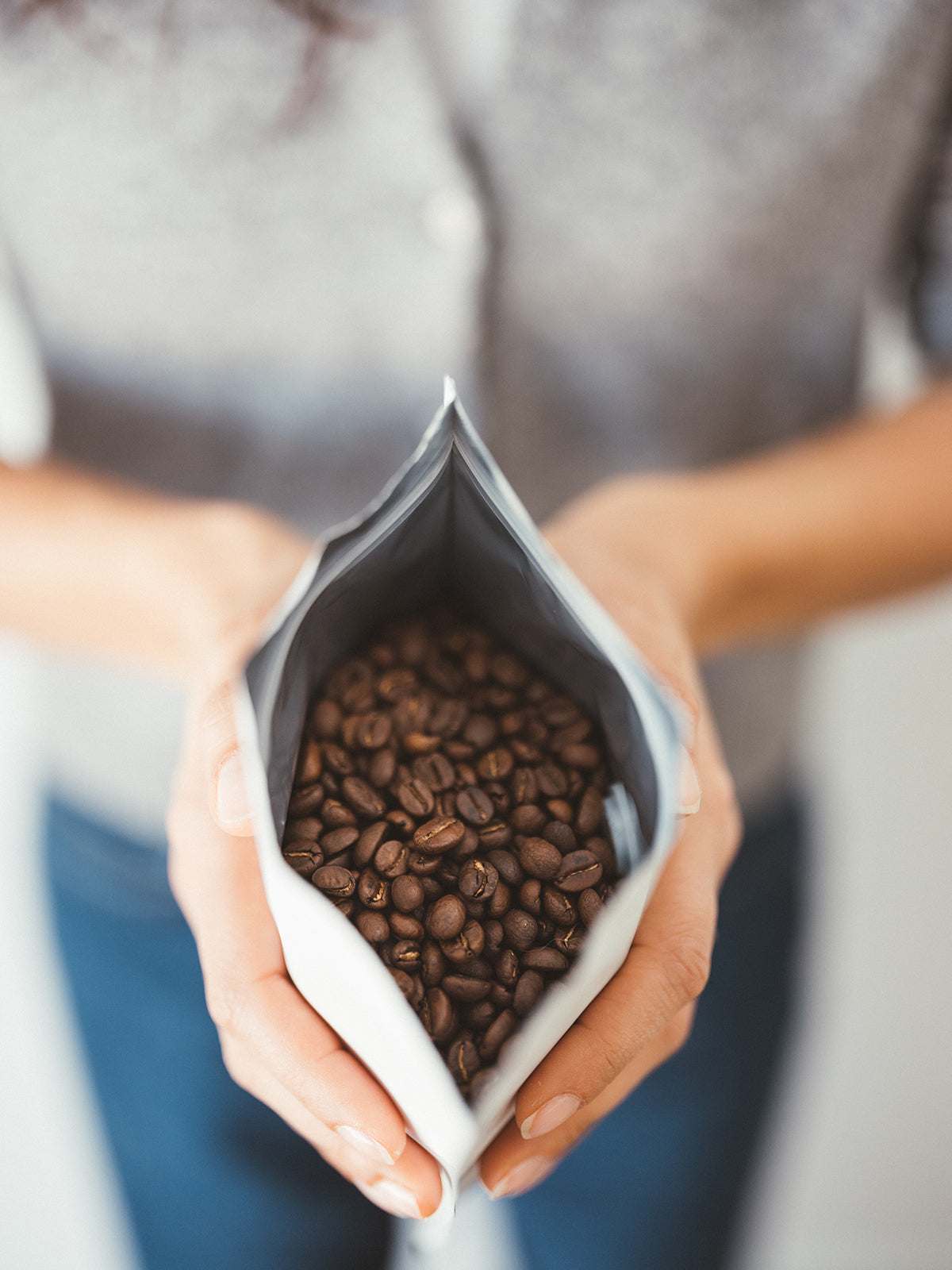 Close-up of a person holding an open bag of Shadow Work coffee beans showcasing rich, roasted beans inside.